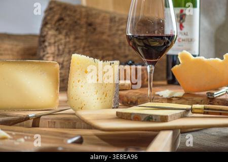 Pezzi di formaggio assortiti e un bicchiere di vino rosso disposti su un tavolo da servizio in legno Foto Stock