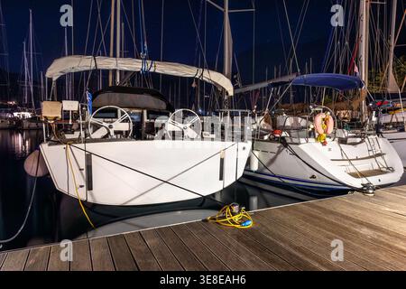 Yacht ormeggiati marina calma notte ponti illuminati riflessi corde d'acqua cavi attrezzature nautiche ambiente tranquillo del porto. Il cielo stellato si staglia Foto Stock
