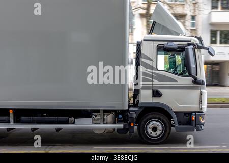 Camion bianco per consegne in strada. Il veicolo commerciale si sposta lungo edifici urbani. Foto Stock