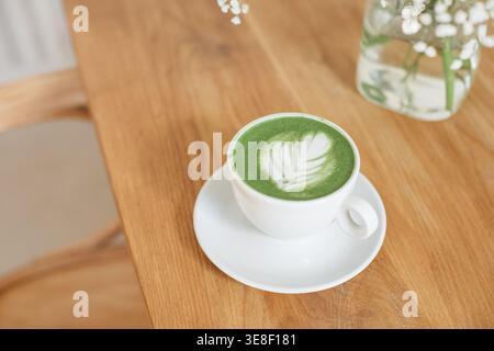 Vista dall'alto ravvicinata di una bevanda calda con latte matcha su un tavolo di legno accanto a un bouquet di fiori in vaso Foto Stock