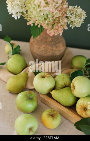 Primo piano di un mucchio di ortensie fresche in una caraffa rustica di argilla su un tavolo con mele su un tagliere di legno Foto Stock