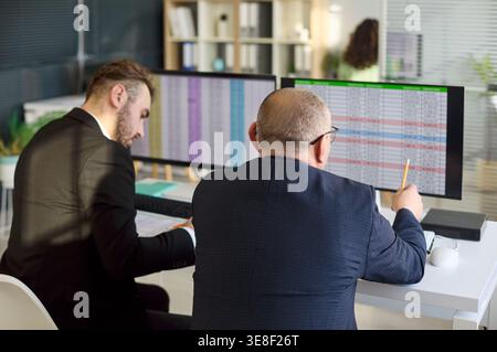 Due uomini d'affari analizzano i fogli di calcolo sugli schermi dei computer durante la riunione d'ufficio Foto Stock