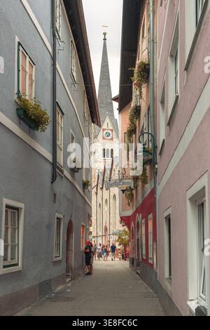 Hallstatt, Austria - 5 agosto 2018: Una stretta strada acciottolata costeggiata da case alpine colorate conduce direttamente a un alto campanile della chiesa, come visitatore Foto Stock