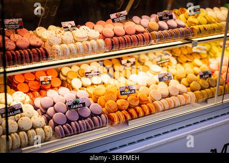 Eine verlockende Auslage mit farbenfrohen Macarons in einer Patisserie a Parigi. Die französischen Feingebäcke sind in verschiedenen Geschmacksrichtungen wie Himbeere, Mango, Cassis und Praline kunstvoll in Reihen angeordnet. Die Warme Beleuchtung der Vitrine hebt die intensiven Farben hervor und vermittelt die elegante Genusskultur der französischen Hauptstadt. *** Un'allettante esposizione di macaron colorati in una pasticceria a Parigi i dolci francesi sono disposti ad arte in file in vari sapori come lampone, mango, cassis e praline la calda illuminazione della vetrina mette in risalto il Foto Stock