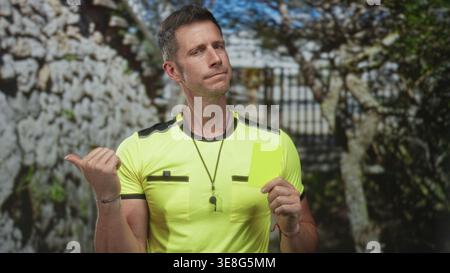 L'uomo punta il pollice e tiene il cartellino giallo accanto al cancello di pietra all'ingresso dell'edificio; sport dell'autorità di applicazione delle regole. Foto Stock