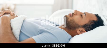Uomo che riposa sul letto con gli occhi chiusi nella luce del mattino durante un momento tranquillo Foto Stock