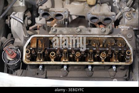 Chiusura di un motore aperto con coperchio delle valvole rimosso che mostra i bilancieri e i depositi pesanti di morchia d'olio, indicando l'usura e i problemi di manutenzione in un fou Foto Stock