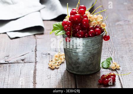 Ribes bianco e rosso in un secchio di metallo su fondo di legno. Foto Stock