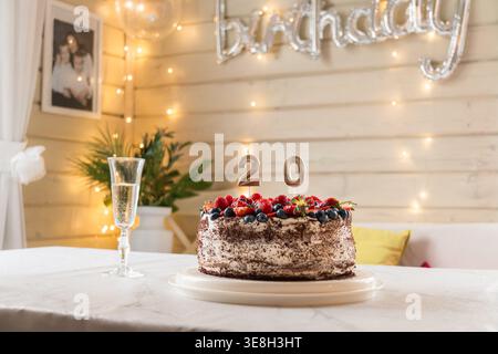 Torta di compleanno con frutti di bosco e numero 20 di candele sul tavolo in un ambiente accogliente con luci calde Foto Stock