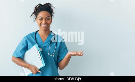 Giovane donna in Scrubs tiene Clipboard e sorrisi in un ambiente medico Foto Stock