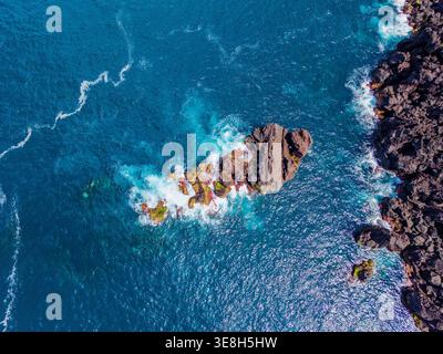 Vista aerea delle aspre e scure rocce vulcaniche che contrastano con il mare turchese, dove le onde bianche schiumose si infrangono intorno alla costa di Prainha, Pico, Foto Stock
