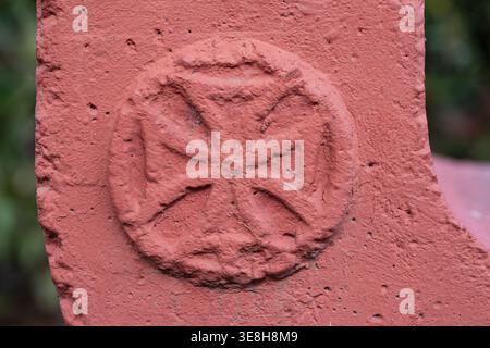 Primo piano di un rilievo a croce Bolnisi dipinto di rosso su una superficie in pietra testurizzata con sfondo bokeh Foto Stock