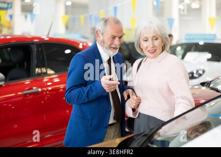 il venditore mostra un'auto a una donna anziana presso una concessionaria Foto Stock