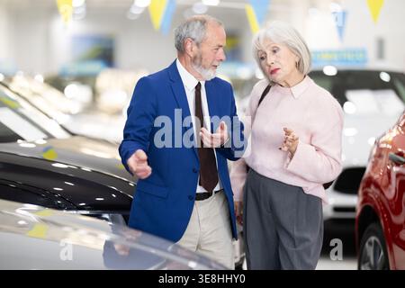 il venditore mostra un'auto a una donna anziana presso una concessionaria Foto Stock