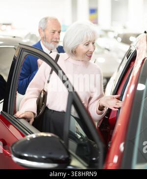 il venditore mostra un'auto a una donna anziana presso una concessionaria Foto Stock