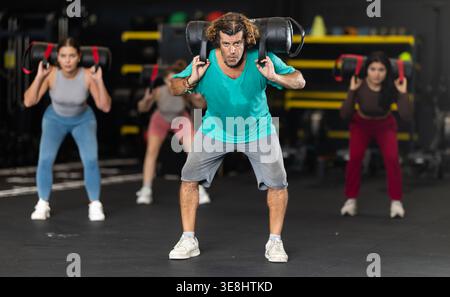Uomo di mezza età determinato che esegue squat con sacchi di sabbia Foto Stock