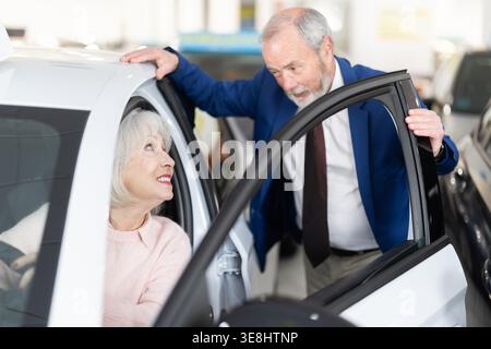 il venditore mostra un'auto a una donna anziana presso una concessionaria Foto Stock