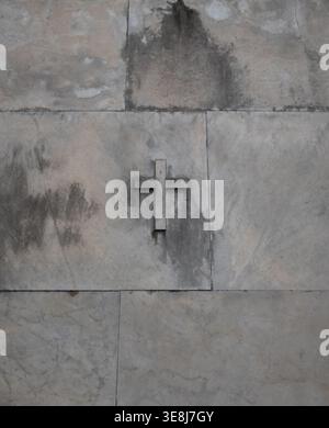 muro in blocchi di marmo nel cimitero con piccola croce in marmo grigio medio o pietra o cemento verticale sfondo religioso o retro Foto Stock
