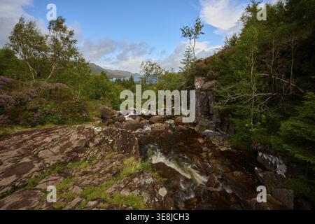 L'acqua scorre sulle rocce in una zona boscosa sotto il cielo azzurro, cascate Victoria, Slattadale, Achnasheen, Scozia, Regno Unito, Gran Bretagna Foto Stock