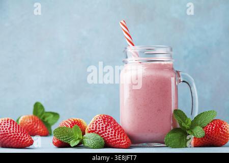 Frullato di fragole o frullato nel barattolo mason sul tavolo turchese. Cibo sano per colazione e spuntino Foto Stock