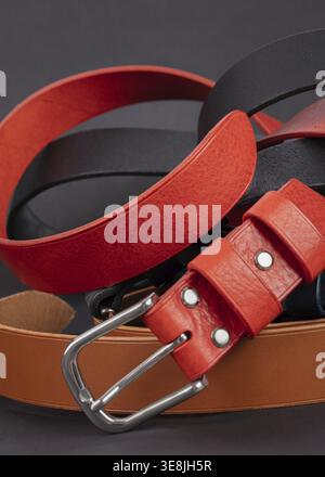 Parte della cintura in pelle rossa con fibbie in metallo primo piano su sfondo grigio scuro Foto Stock