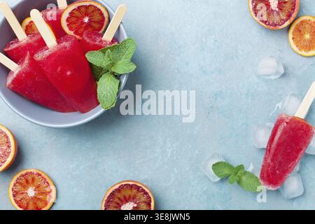 Gelato agli agrumi fatto in casa o papaveri decorati con foglie di menta verde e fette di arancia sulla vista del tavolo blu. Succo di frutta congelato. Cibo estivo Foto Stock
