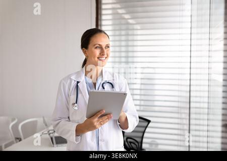 Medico donna in possesso di tablet digitale in piedi nello studio medico Foto Stock