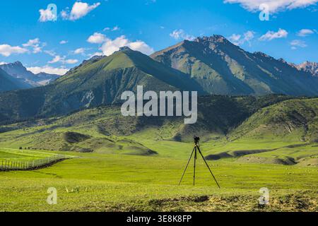 La fotocamera montata sul treppiede cattura vasti paesaggi montuosi. I campi erbosi si estendono sotto il cielo azzurro, creando una pittoresca scena all'aperto. Foto Stock