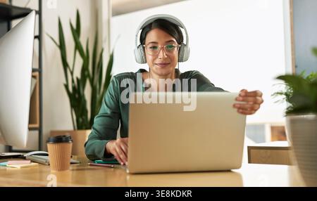 Donna felice, giornalista o cuffie con laptop in ufficio per ascoltare musica, trasmettere online o fare report. Donna, dipendente o in ascolto al computer Foto Stock