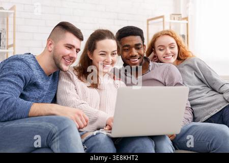 Gruppo di amici che si divertono insieme mentre guardano qualcosa su un notebook in interni Foto Stock