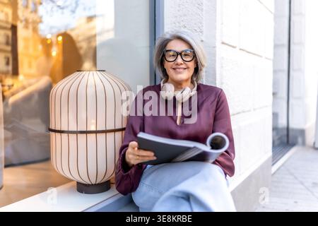 Donna matura sorridente rilassante leggendo libri strada Foto Stock