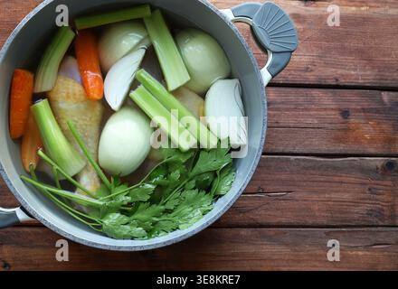 Preparare il tradizionale brodo di pollo con ingredienti biologici freschi in una pentola grigia su sfondo rustico. Concetto di cucina sana. Primo piano. Copia spazio Foto Stock