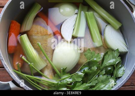 Preparare il tradizionale brodo di pollo con ingredienti biologici freschi in una pentola grigia su sfondo rustico. Concetto di cucina sana. Primo piano. Copia spazio Foto Stock