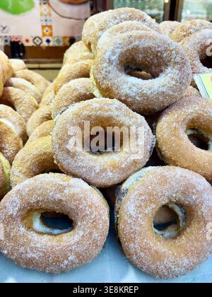 Primo piano di ciambelle fritte tradizionali italiane ricoperte di zucchero (Ciambelle o Graffe) impilate su un vassoio in una panetteria. Colazione dolce con zucchero granulato. Foto Stock