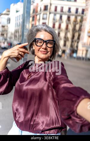 Donna matura sorridente che tiene il caffè scattando un selfie Foto Stock
