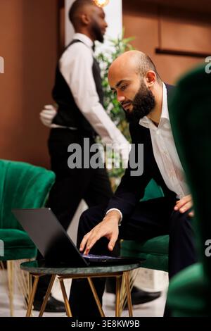Uomo d'affari del Medio Oriente in tuta per prepararsi a partecipare a una conferenza ufficiale con il Consiglio di amministrazione, a un viaggio d'affari. Giovane imprenditore che lavora su un computer portatile nell'area lounge, riunione di gestione. Foto Stock