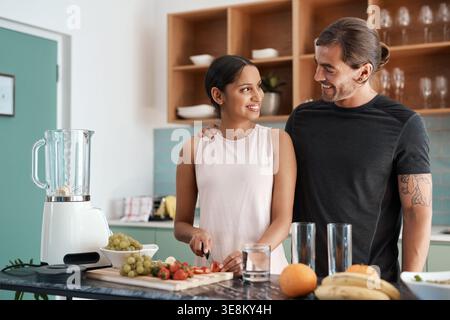 Coppia, frullato e felice con frutta in cucina casalinga per salute, benessere e nutrizione nella dieta. Rapporto interrazziale, persone e partner tagliati Foto Stock