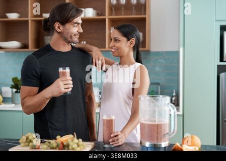 Coppia, frullato e felice in cucina casalinga per uno stile di vita sano, benessere e nutrizione nella dieta. Relazione interrazziale, persone e partner Foto Stock