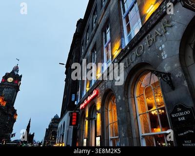 Edimburgo, Scozia, Regno Unito - 16 febbraio 2026: Scena urbana serale della facciata del Waterloo Bar con luci calde e torre dell'orologio distante a Edimburgo, S. Foto Stock