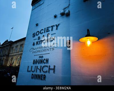 Edimburgo, Scozia, Regno Unito - 16 febbraio 2026: Scritta vintage a parete per il brunch, il pranzo e la cena accanto a un caldo lampione ambra in serata a Edimburgo. Foto Stock