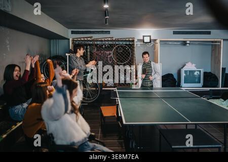 Gli studenti giocano a ping pong mentre gli amici fanno il tifo in una sala ricreativa informale Foto Stock