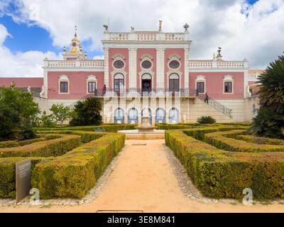 Palazzo rococò rosa di Estoi nella regione dell'Algarve in Portogallo, caratterizzato da un giardino formale con siepi e fontana sotto un cielo nuvoloso Foto Stock