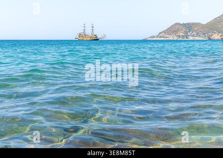 Una nave turistica a tema pirata naviga all'orizzonte del blu brillante del Mar Mediterraneo ad Alanya, Turchia. L'acqua che ondeggia su un fondale roccioso Foto Stock