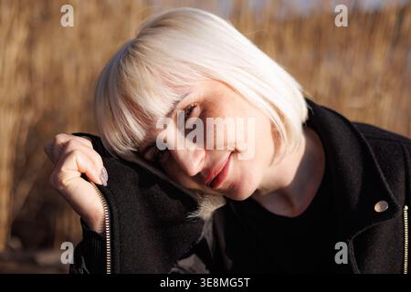 Una bella giovane donna con un sorriso dolce ha allontanato il viso dai bassi raggi del caldo sole primaverile. Una bionda con lentiggini sul viso. Foto Stock