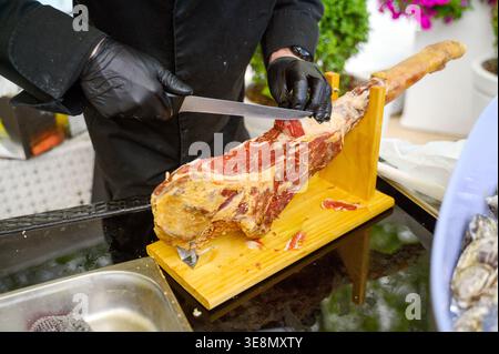 Affettare a mano il prosciutto stagionato a secco mostrando la sua splendida consistenza marmorizzata con una lama lunga. Concetto di artigianato culinario professionale, autentico europeo Foto Stock