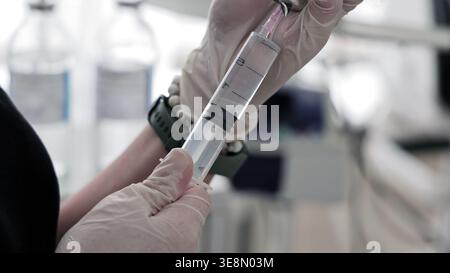 Primo piano preparazione della siringa medica in clinica. Le mani con i guanti tengono in mano una siringa mentre si estrae la medicina liquida in un ambiente clinico, mostrando l'assistenza sanitaria Foto Stock