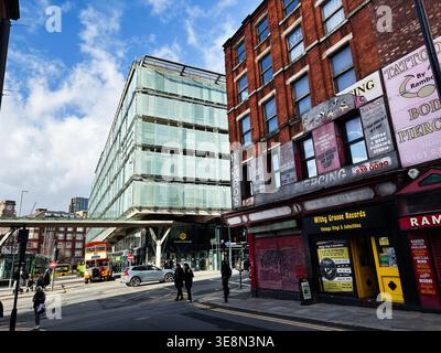Manchester, Regno Unito - 22 febbraio 2026: Contrasto urbano tra architettura contemporanea in vetro e storici negozi in mattoni a Manchester, Regno Unito con autobus e Foto Stock