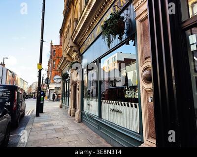 Manchester, Regno Unito - 22 febbraio 2026: Storico negozio con vetrine e pedoni su una strada soleggiata di Manchester, Regno Unito. Foto Stock