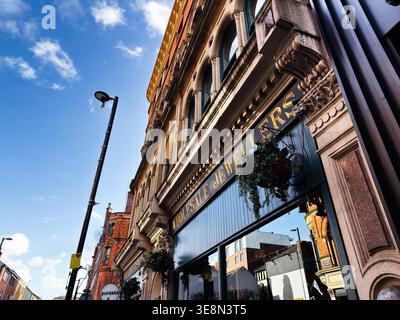 Manchester, Regno Unito - 22 febbraio 2026: Gioielleria vittoriana all'ingrosso ornata a Manchester Regno Unito con fioriere appese, cielo blu e riflessi. Foto Stock