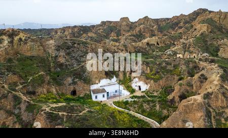 Vista dall'alto delle iconiche case rupestri di Guadix. Facciate bianche e tetti piastrellati sono annidati in aspre colline di argilla, collegate da tortuosi sentieri amon Foto Stock